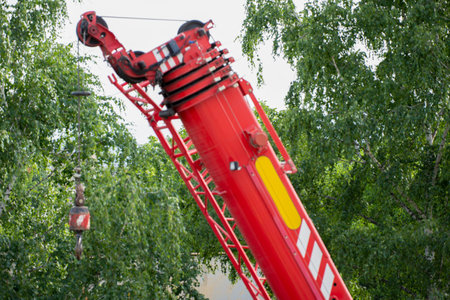 A red construction crane is actively lifting materials above a green landscape urban. The surrounding trees provide a contrast against the bright machinery under a clear sky.の写真素材