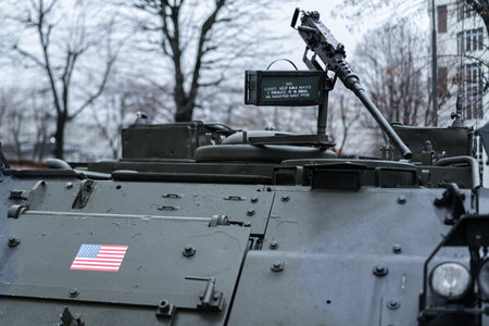 A military vehicle equipped with a mounted gun showcases the American flag while stationed in an urban area amid bare trees on a winter day.の写真素材