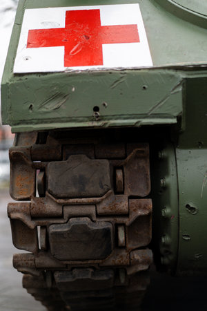 An armored vehicle features a red cross emblem prominently displayed on its side. The focus is on the durable tracks and weathered surface, set against a city backdrop during daytime.の写真素材
