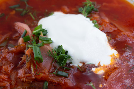 A bowl of vibrant red borscht is beautifully garnished with a dollop of sour cream and chopped fresh...