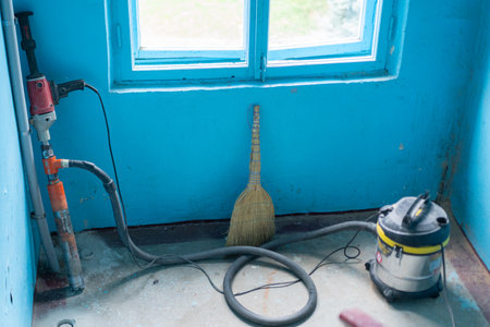 A broom and a vacuum cleaner are positioned near a window in a newly renovated bright blue room. The space is partially cleaned and ready for the final touches.の写真素材