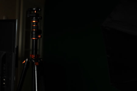 A sturdy tripod stands tall in a dark studio, illuminated by subtle light highlighting its features. Nearby equipment suggests preparation for a creative photography session.の写真素材