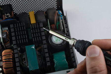 An individual is skillfully working on electronic components, applying a soldering iron to repair circuit boards in a well-organized workshop. Tools and parts are visible.の写真素材