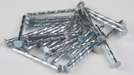 Metallic finishing nails lie haphazardly on a smooth white surface. These nails are essential for various construction tasks, offering a strong hold for woodworking applications.の写真素材