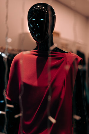 A sleek mannequin showcases a striking red garment in a contemporary retail setting, surrounded by a stylish backdrop. Shoppers pass by, admiring the fashion display.の写真素材