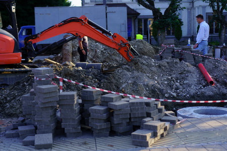 Two construction workers are engaged in laying bricks while heavy machinery operates nearby on a...