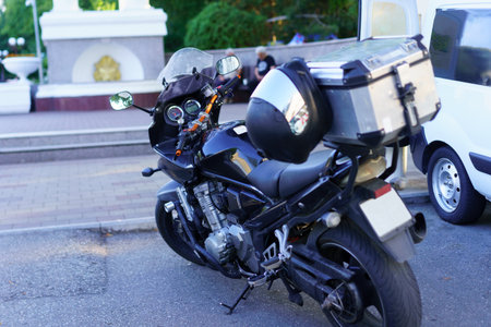 A black motorcycle with a shiny rear trunk is parked next to a white van. The surrounding area is...