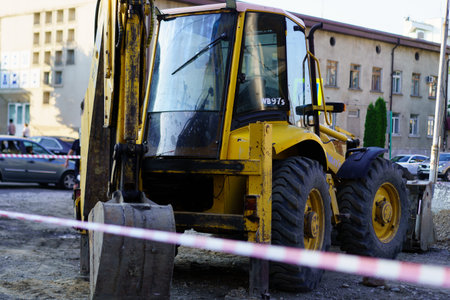 Construction activity takes place at an urban site where a yellow backhoe loader is parked. It is...