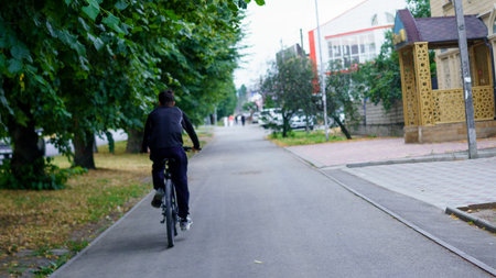 A young person cycles on a smooth path lined with trees in a peaceful residential area, showing the tranquility of urban life during the late afternoon.の写真素材