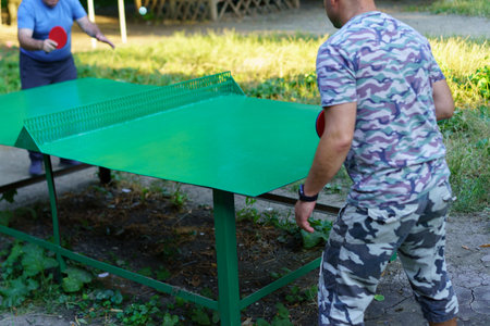 Players compete in a lively table tennis game at a sunny outdoor location, surrounded by greenery and enjoying the recreational activity together.の写真素材