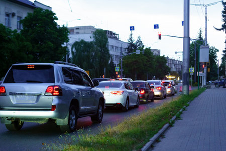 Vehicles line up on a busy city street as dusk settles, with traffic signals illuminating the surroundings. The scene captures the typical evening rush hour atmosphere.の写真素材