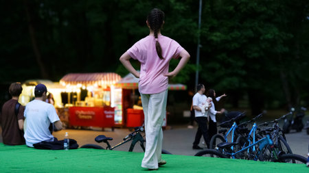 A child stands confidently on a platform in a park as people relax nearby. Food stalls are visible in the background, creating a lively summer atmosphere.の写真素材