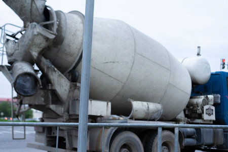A concrete mixer truck sits beside a fenced area at a construction site, with dusk falling and construction lights illuminating the surroundings.の写真素材
