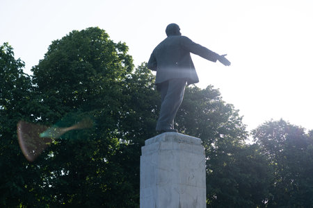 A statue of a historical leader stands on a pedestal in a lush green park. Sunlight shines brightly,...
