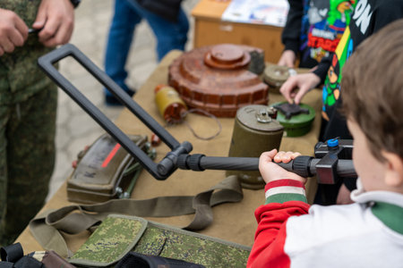 At a community event in a public park, a child engages with military equipment while a guide...