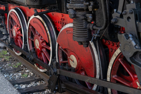 Close-up view of the steel wheels of a vintage steam locomotive, featuring vibrant red accents and...