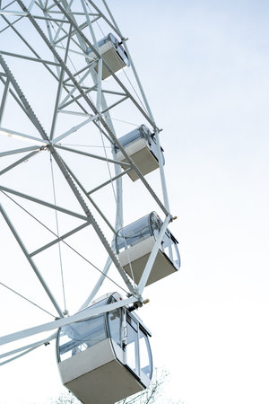 Ferris wheel cabins ascend toward the sky in an amusement park surrounded by trees, showcasing a bright and sunny daytime atmosphere filled with excitement.の写真素材