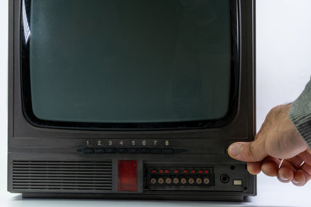 A hand is pressing the power button of a vintage television, which features knobs and buttons on its front panel. This model reflects classic design elements from the past.の写真素材