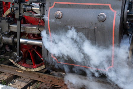 The powerful steam engine exudes clouds of vapor, showing its mechanical beauty and historical importance. The railway setting enhances its vintage charm in the afternoon light.の写真素材