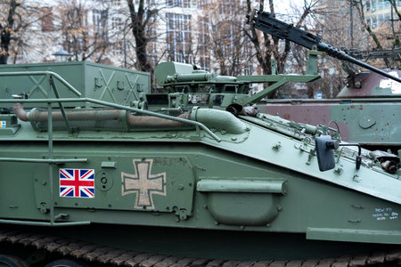 A British armored vehicle features prominently at a military exhibition. It is surrounded by trees with budding leaves, showing a blend of history and modernity in a bustling urban setting.の写真素材