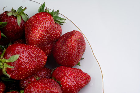 Juicy red strawberries are piled high in a white bowl, showing off their vibrant color and texture. Sunlight softly illuminates the scene, enhancing the freshness of the fruit.の写真素材