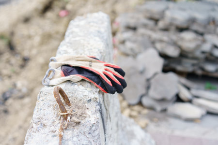 A pair of safety gloves lies on a concrete block amid construction debris. The setting reveals...
