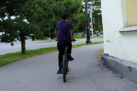 A young man is cycling along a smooth path lined with trees, enjoying the peaceful atmosphere of the...