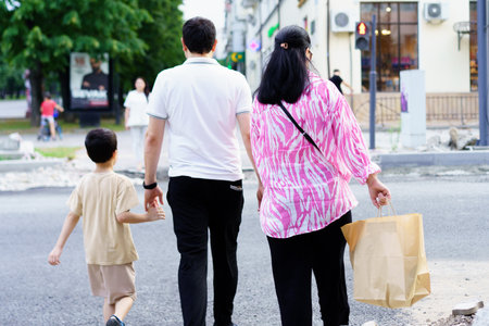 Three individuals walk together in an urban environment, enjoying their time. One adult carries a...