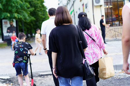 A group of individuals strolls along a city street on a warm summer day. Children and adults...