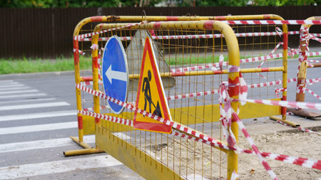Construction barriers are positioned across the road at an intersection. Safety signs indicate...