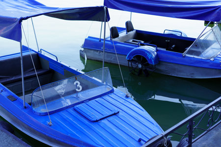 Two blue boats sit peacefully at a dock on a serene lake, reflecting the early morning light while...