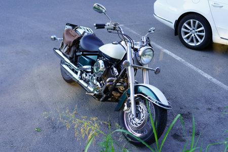 A sleek classic motorcycle sits parked at the roadside, showcasing a polished chrome finish and a leather bag attached. Evening light enhances its appeal among the cars nearby.の写真素材