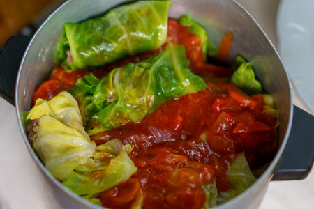 Cabbage rolls filled with meat and rice are cooking in a pot, topped with vibrant red tomato sauce. The dish showcases fresh produce and enhances comfort food traditions.の写真素材