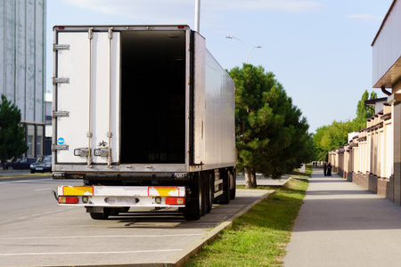 A large white delivery truck is parked on the side of a city street. It is positioned next to a...