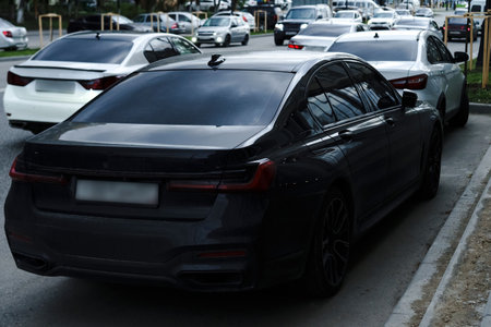 Several high-end vehicles are parked along a bustling city street in the late afternoon. The urban...