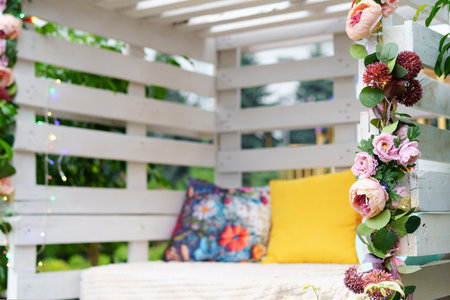 Bright and inviting outdoor seating area features colorful cushions and pink flowers. The wooden structure is surrounded by greenery, creating a peaceful atmosphere for relaxation.の写真素材