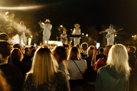A group of musicians perform on stage under bright lights while an enthusiastic crowd watches and...