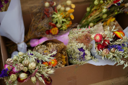 Bright and diverse dried flower bouquets are carefully arranged in a cardboard box. This scene takes place at a local market in the fall, showing vibrant colors and textures.の写真素材