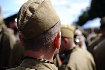 A group of soldiers in vintage military uniforms is seen from behind, standing together during a...