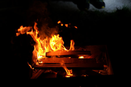 A vibrant fire crackles and glows in a backyard pit as friends and family gather around, enjoying a cool evening under the night sky. The warm light from the flames creates a cozy atmosphere.の写真素材