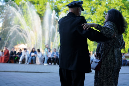 Elderly couple enjoys a dance near a fountain while a small crowd watches and takes delight in the lively atmosphere of a community gathering on a bright day.の写真素材