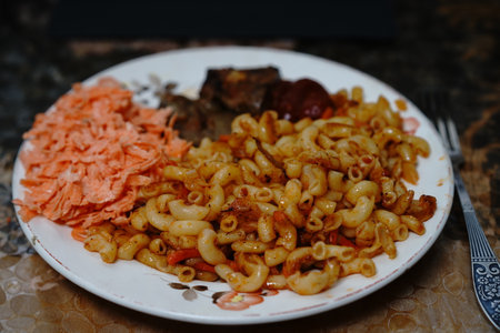 A hearty plate features curly pasta mixed with spices, along with shredded salmon and slices of beef. This satisfying meal is enjoyed at home during a cozy evening.の写真素材