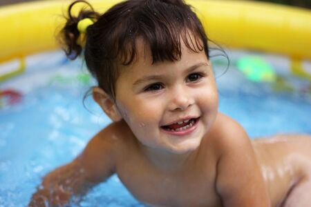 portrait of a happy smiling little girl in a blow up swimming poolの写真素材