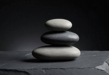 A serene composition featuring three smooth stones stacked on a dark slate surface, perfect for conveying tranquility and balance in design projects.の素材