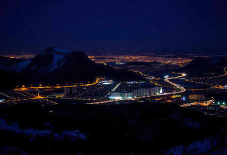 This stunning night view showcases a mountain landscape illuminated by city lights, with a starry sky above. The scene captures urban tranquility amidst nature's beauty.の素材