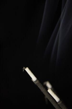 Close-up image of incense sticks burning against dark background の写真素材