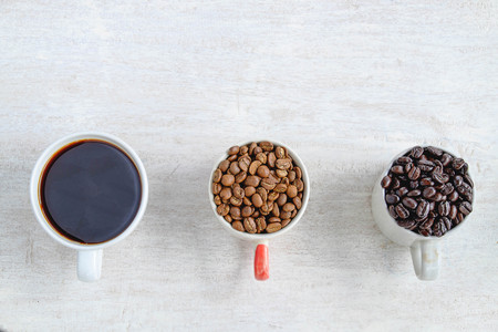 A cup of coffee and a cup of coffee beans on a white wooden floor.