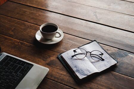 A coffee cup on the desk that has glasses and a notebook computerの写真素材