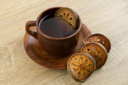 Hot dried bael tea in a wooden cup with dried bael slices