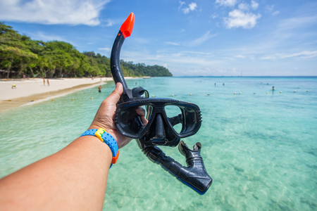 Hand man holding snorkel goggles against beach and skyの写真素材